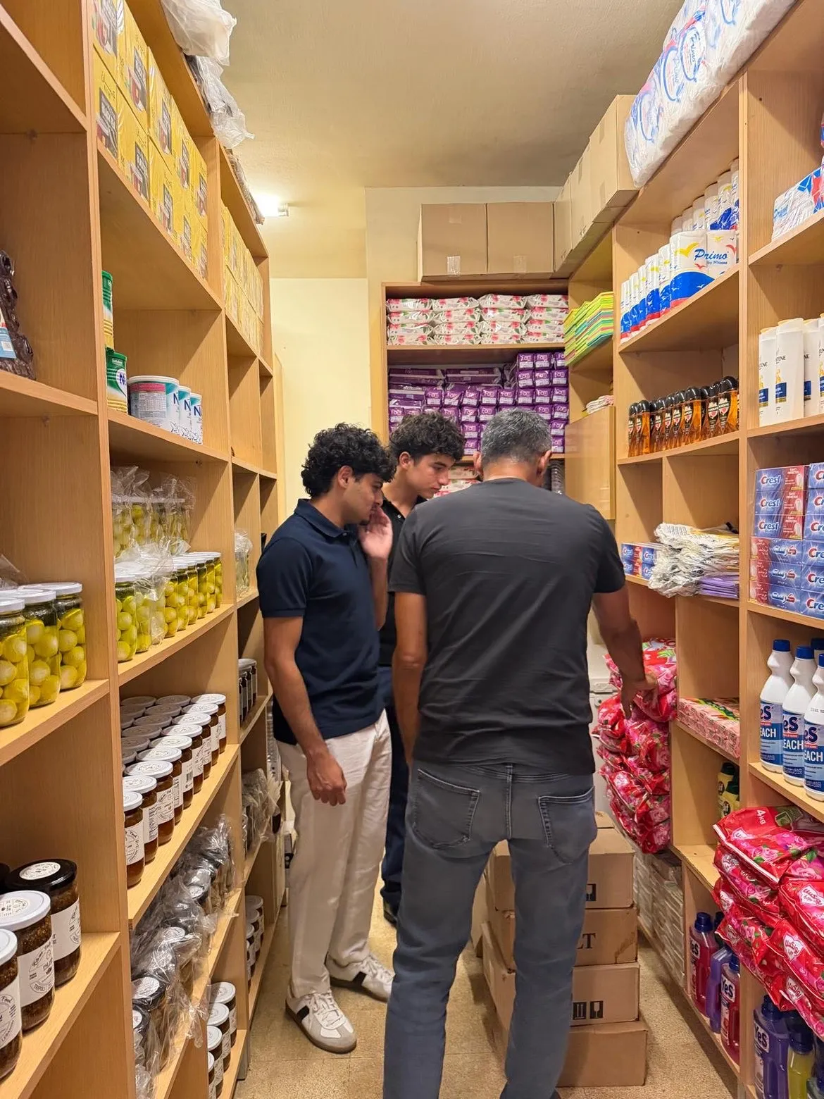 Two Lights for Lebanon students and a Beit el Baraka team member in an aisle of jars and supplies.