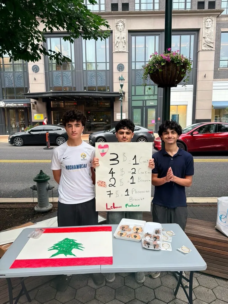 Students holding the Lebanese Fundraiser price sign behind their bake sale table at Pike and Rose.